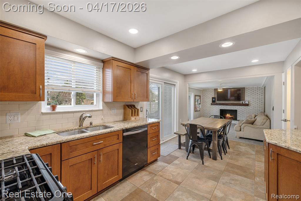 Kitchen with wood finish cabinets, open floor plan, a fireplace, light stone countertops, and recessed lighting