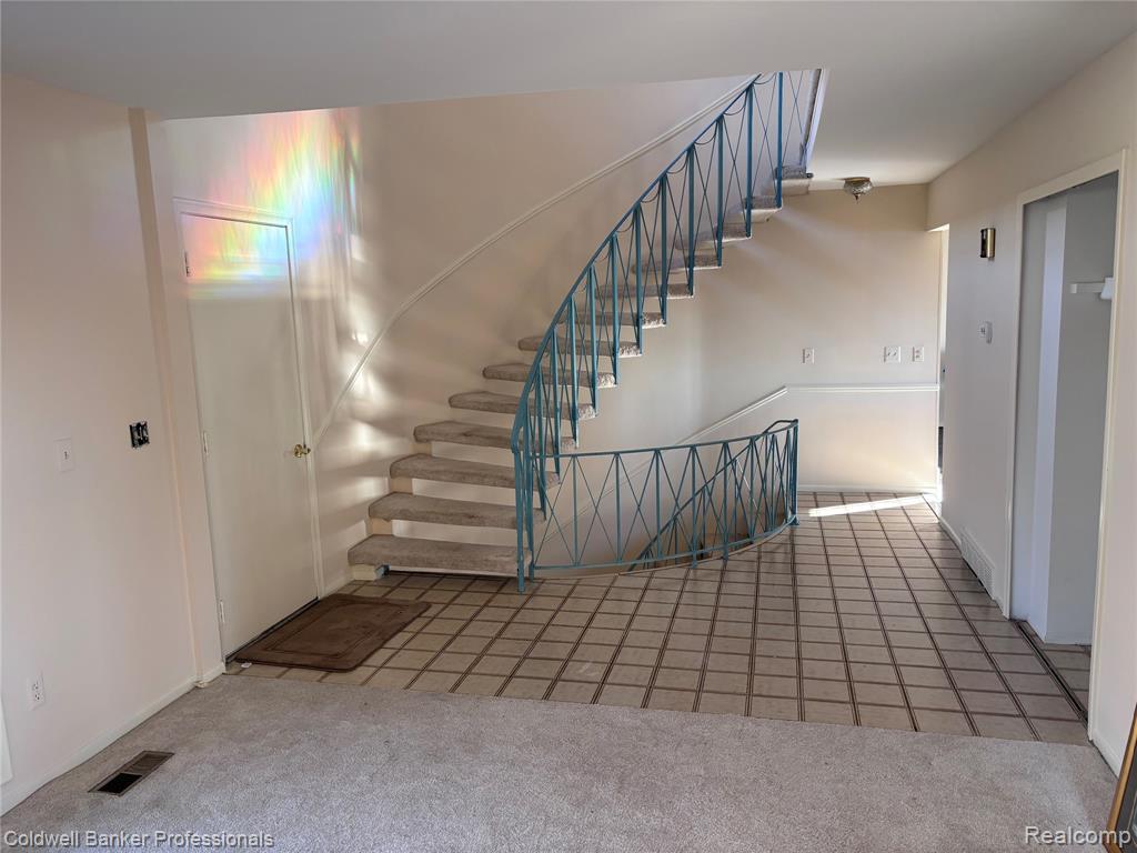 Staircase with carpet floors and tiled foyer