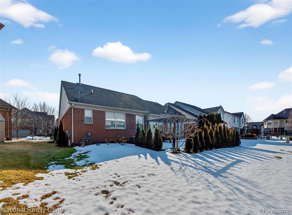 Snow covered rear of property with brick siding and a residential view