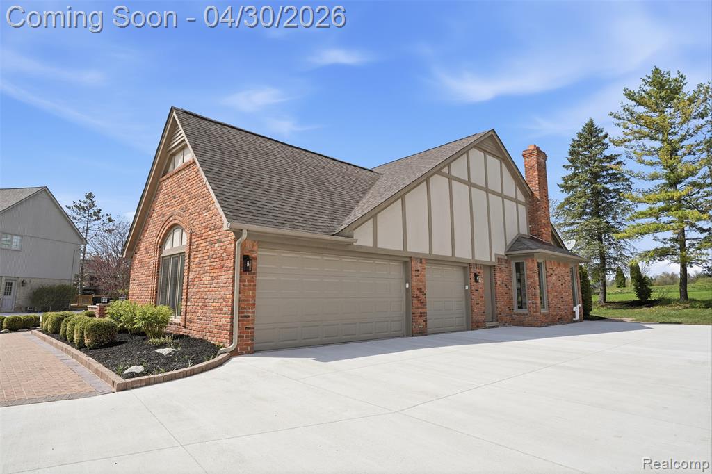 View of property exterior featuring brick siding, a 3 car attached garage, side door entrance, and new concrete driveway