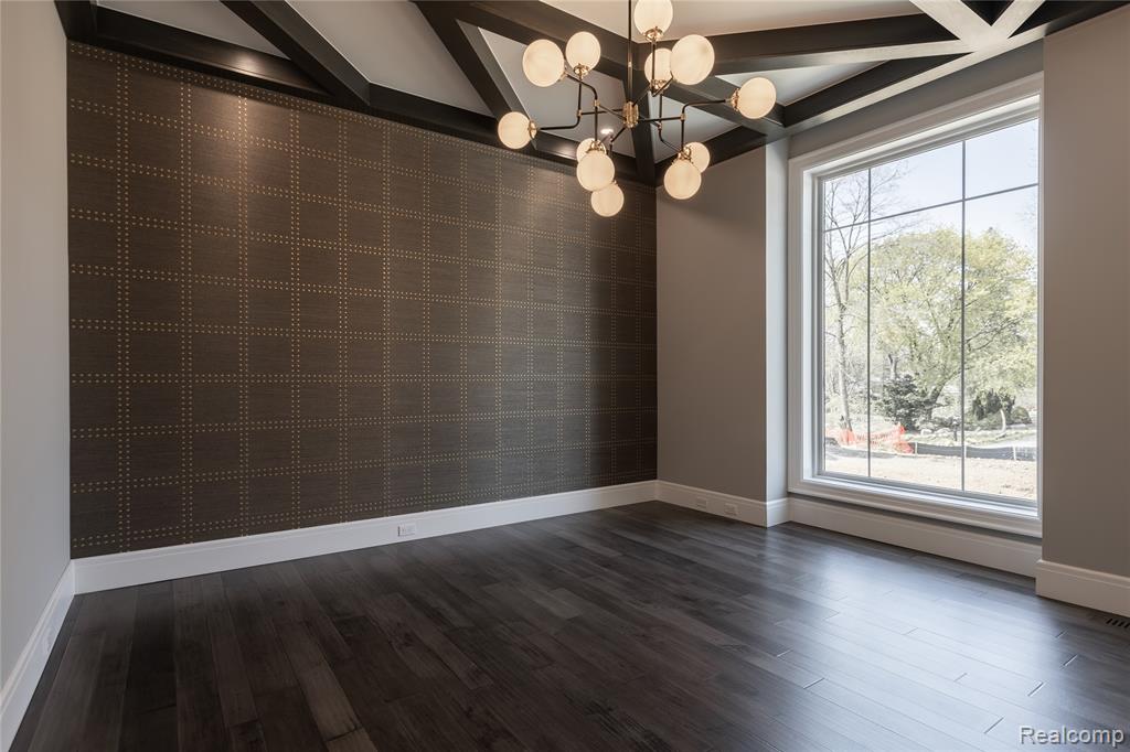 Unfurnished dining area featuring an accent wall, dark wood-type flooring, suspended lighting, wallpapered walls, and coffered ceiling