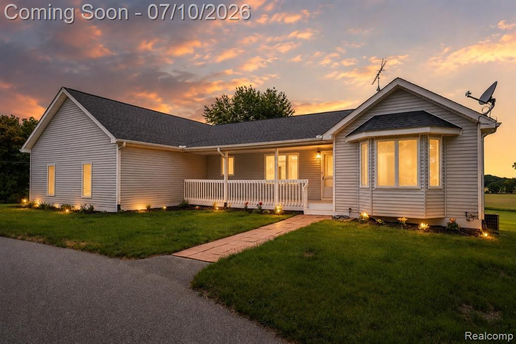 Ranch-style residence featuring light-colored siding, a dark shingle roof, and a covered porch with white railing