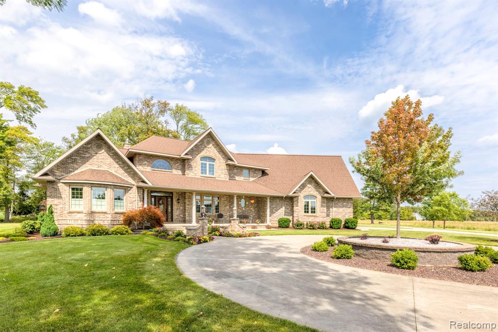 Brick facade residence featuring a covered front porch, arched and bay windows, a circular drive, and mature landscaping