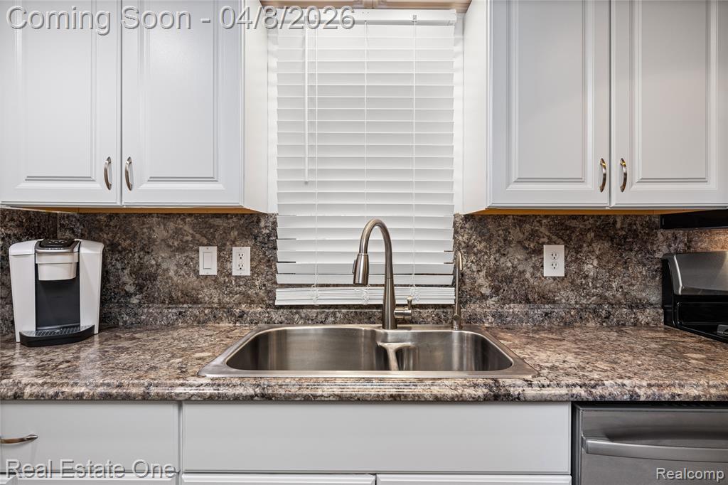 Kitchen with white cabinets, dishwasher, dark stone counters, and backsplash