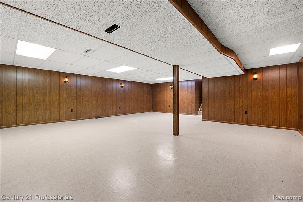 Finished below grade area featuring light floors, wood walls, and a drop ceiling