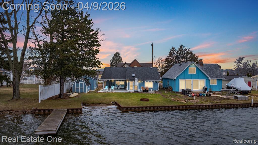 Back of house at dusk featuring a patio, a water view, a storage unit, board and batten siding, and a fire pit