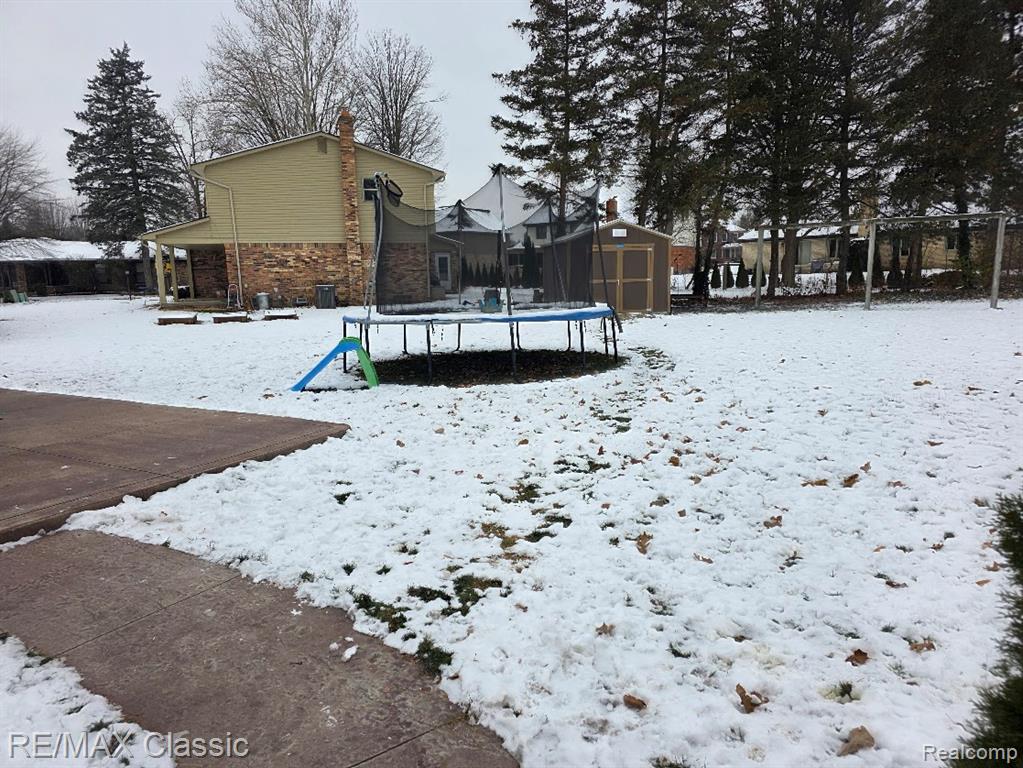 Snowy yard featuring a trampoline and a storage shed