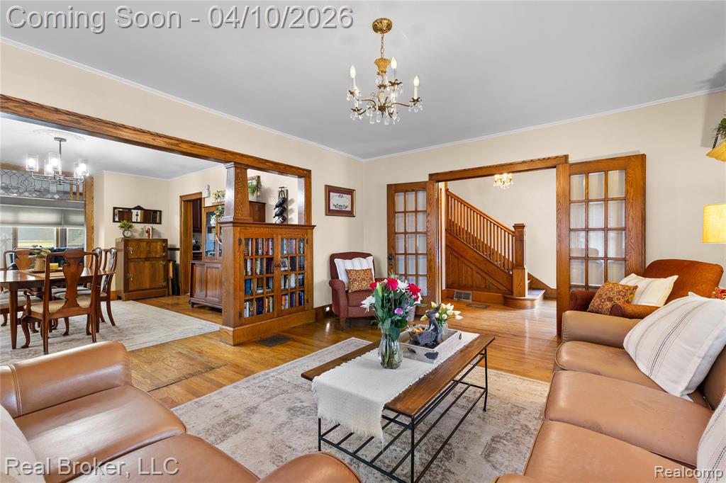 Living room with hanging lights, wood finished floors, and ornamental molding
