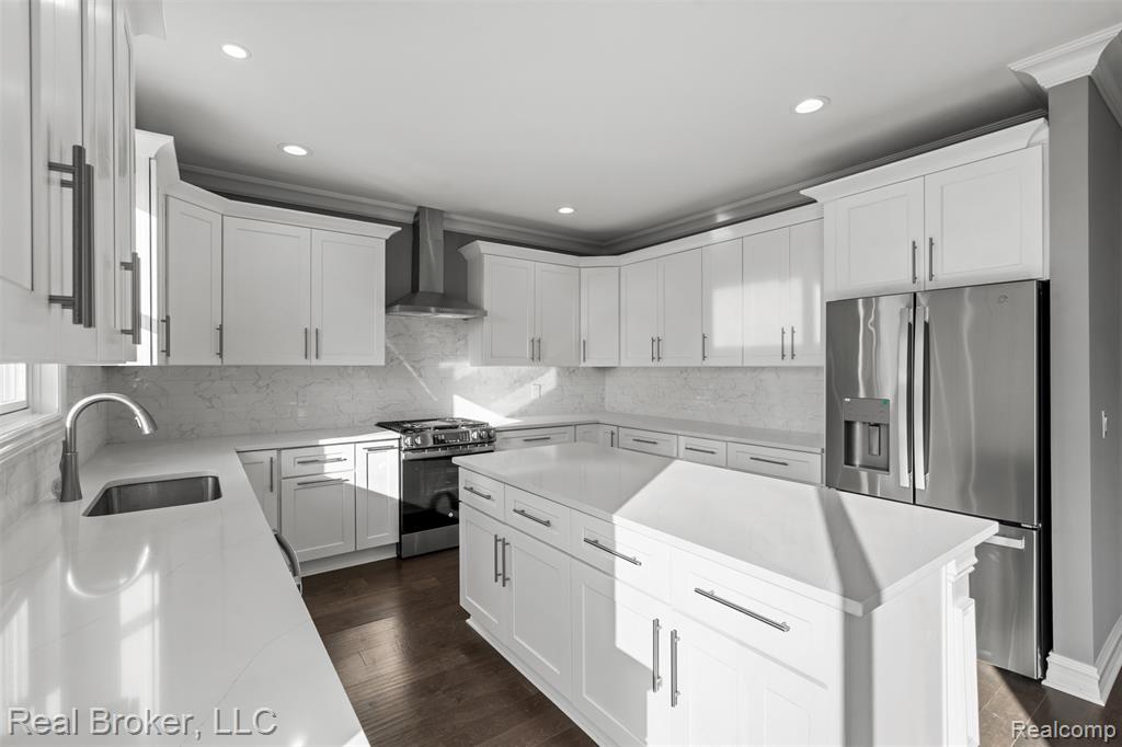 Kitchen with appliances with stainless steel finishes, white cabinetry, a kitchen island, wall chimney range hood, and recessed lighting