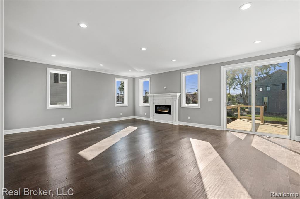Unfurnished living room with ornamental molding, recessed lighting, a glass covered fireplace, and dark wood-type flooring