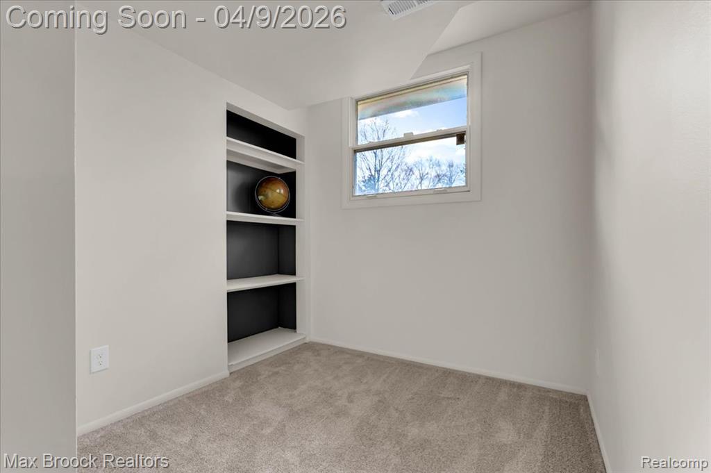 Spare room featuring built in shelves and light colored carpet