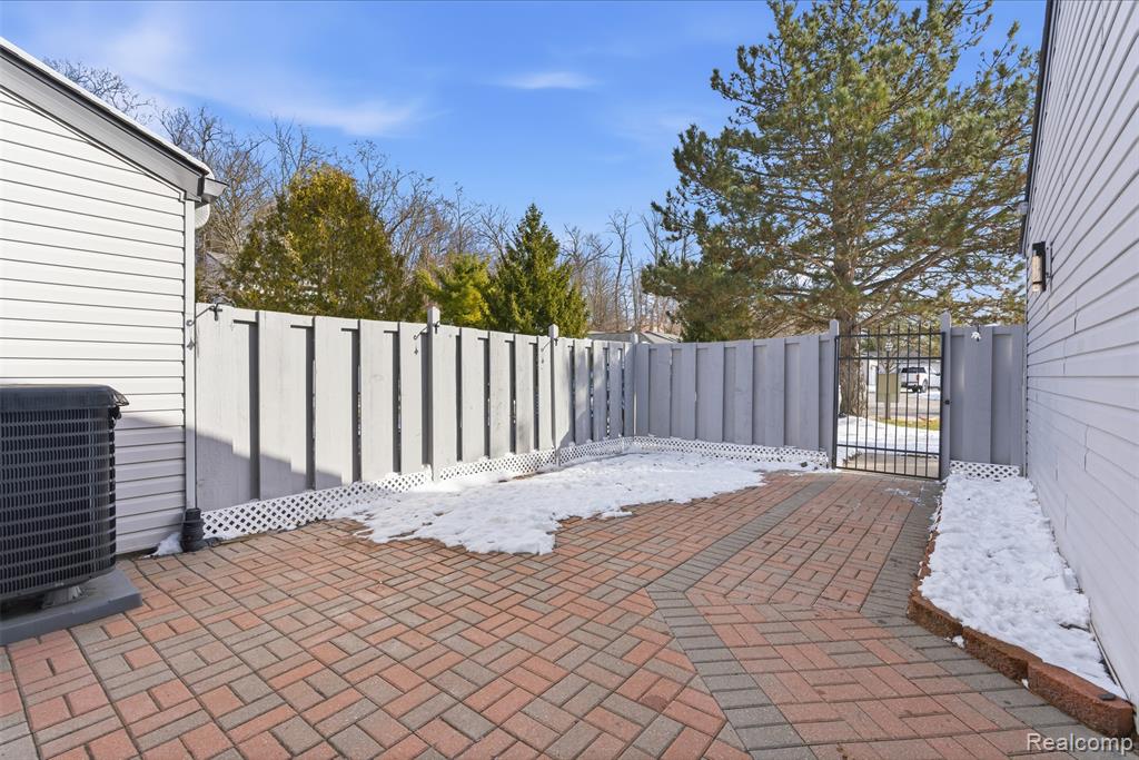 Snow covered patio featuring a patio, a fenced backyard, and a gate