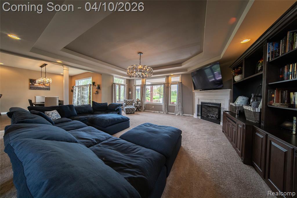 Living room with suspended lighting, a raised ceiling, a fireplace, carpet, and decorative columns