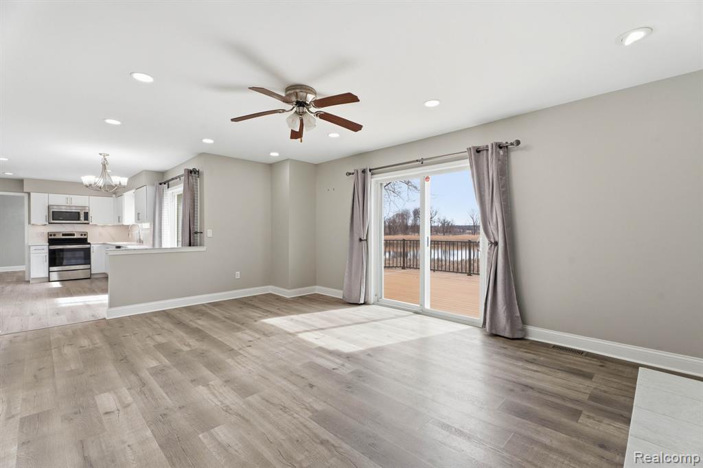 Unfurnished living room with ceiling fan, a chandelier, light wood-type flooring, and a water view