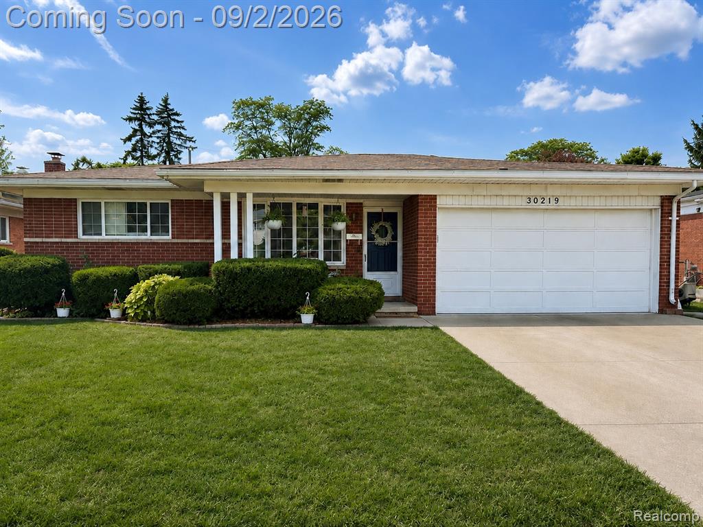 Charming brick ranch home featuring a columned front entrance, manicured landscaping with mature shrubs, expansive driveway, and attached two-car garage