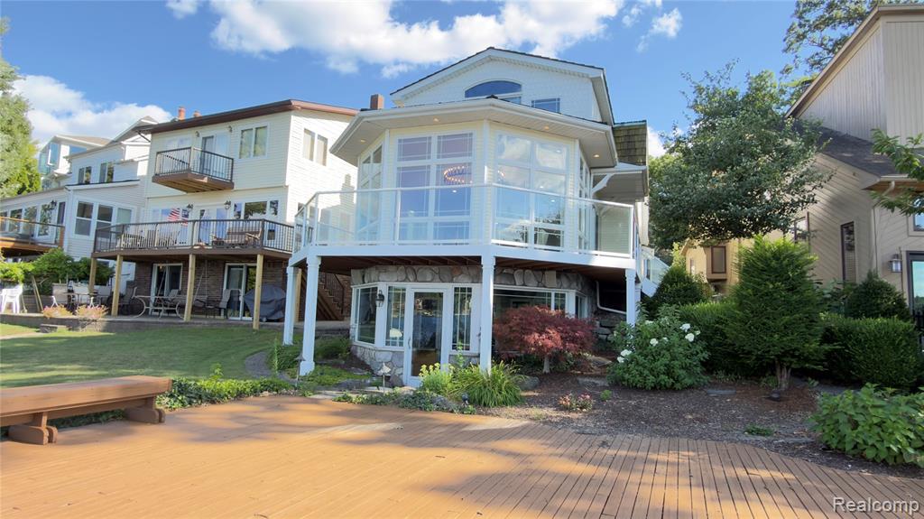 Waterfront property featuring an expansive deck with glass railings, a hexagonal sunroom, and a lower-level sunroom with stone siding