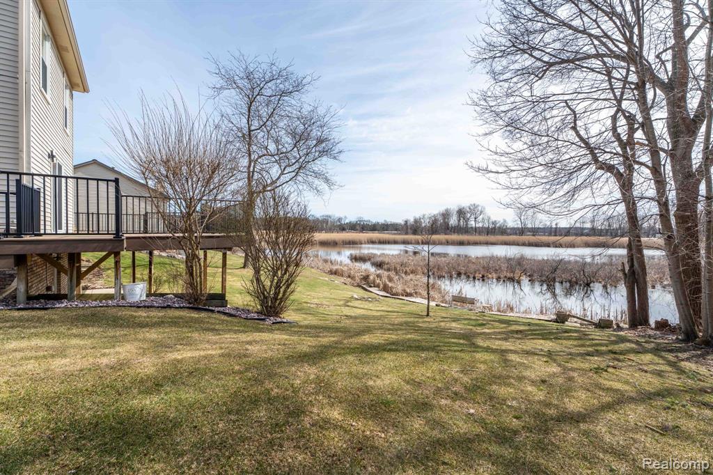 View of grassy yard with a deck with water view and stairs