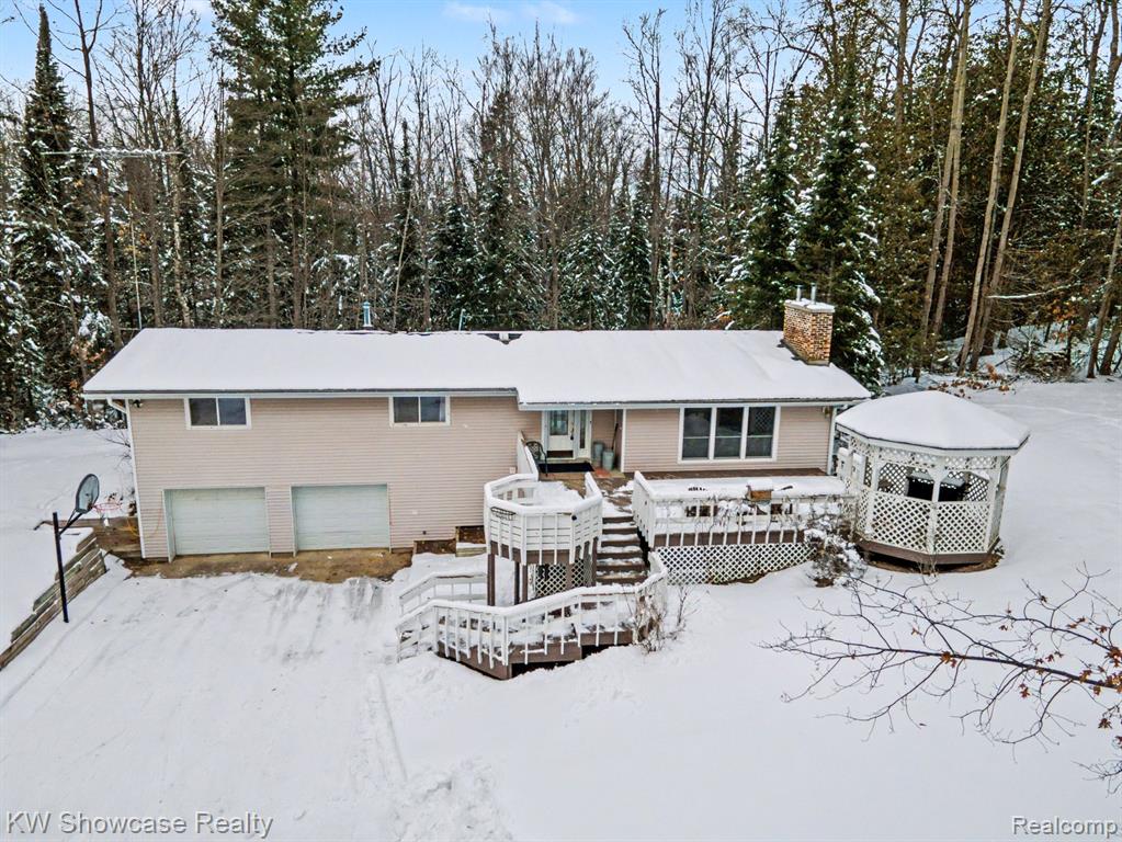 Snow covered rear of property featuring an attached garage, a wooden deck, and a chimney