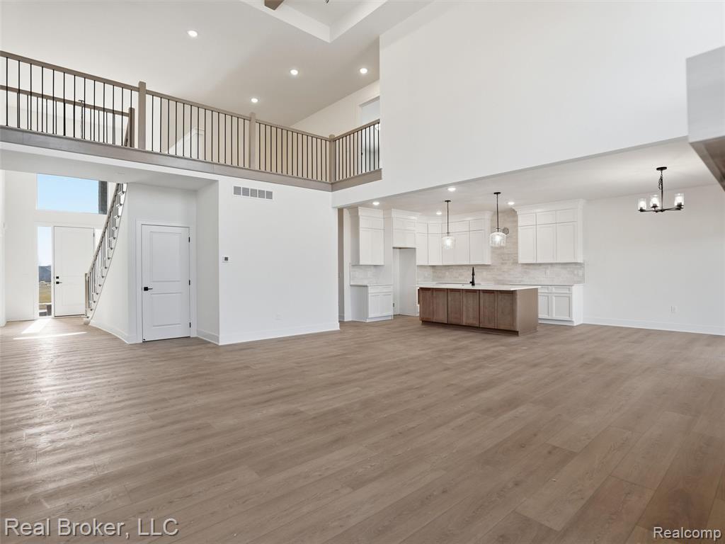 Unfurnished living room with wood finished floors, a high ceiling, suspended lighting, and ceiling fan