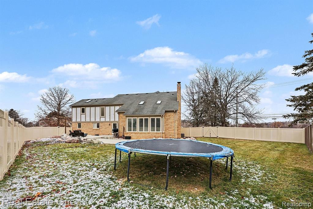Rear view of house featuring a fenced backyard, brick siding, a patio, a trampoline, and a chimney