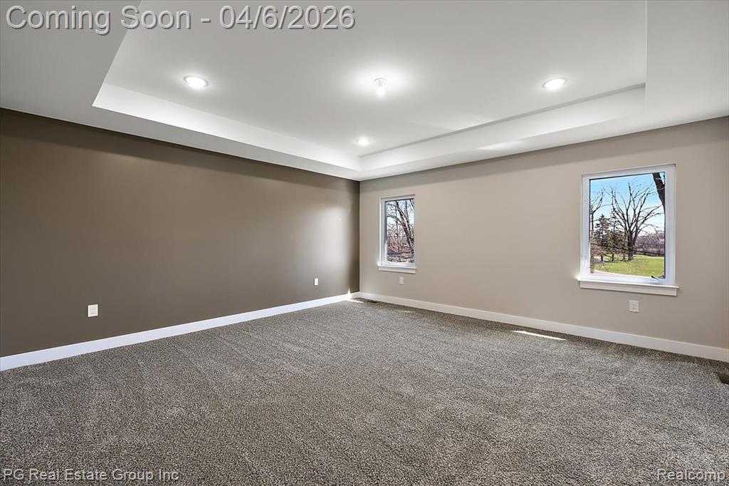 Empty room with a raised ceiling, dark carpet, and recessed lighting