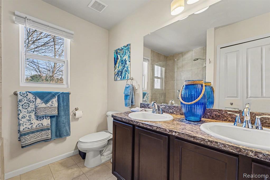 Full bathroom featuring double vanity, tiled shower, and light tile patterned flooring