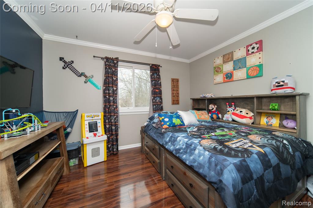 Bedroom with dark wood-type flooring, ornamental molding, and ceiling fan