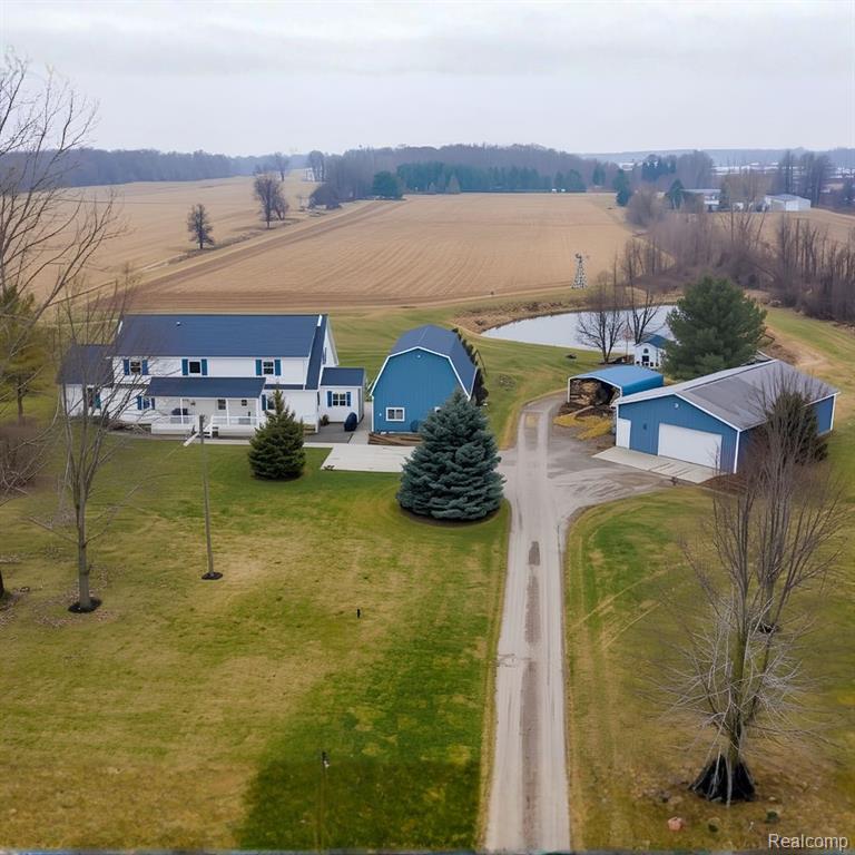 Expansive property featuring a white residence with blue accents, a blue barn, an additional blue outbuilding with a large garage door, a private pond, and a gravel driveway