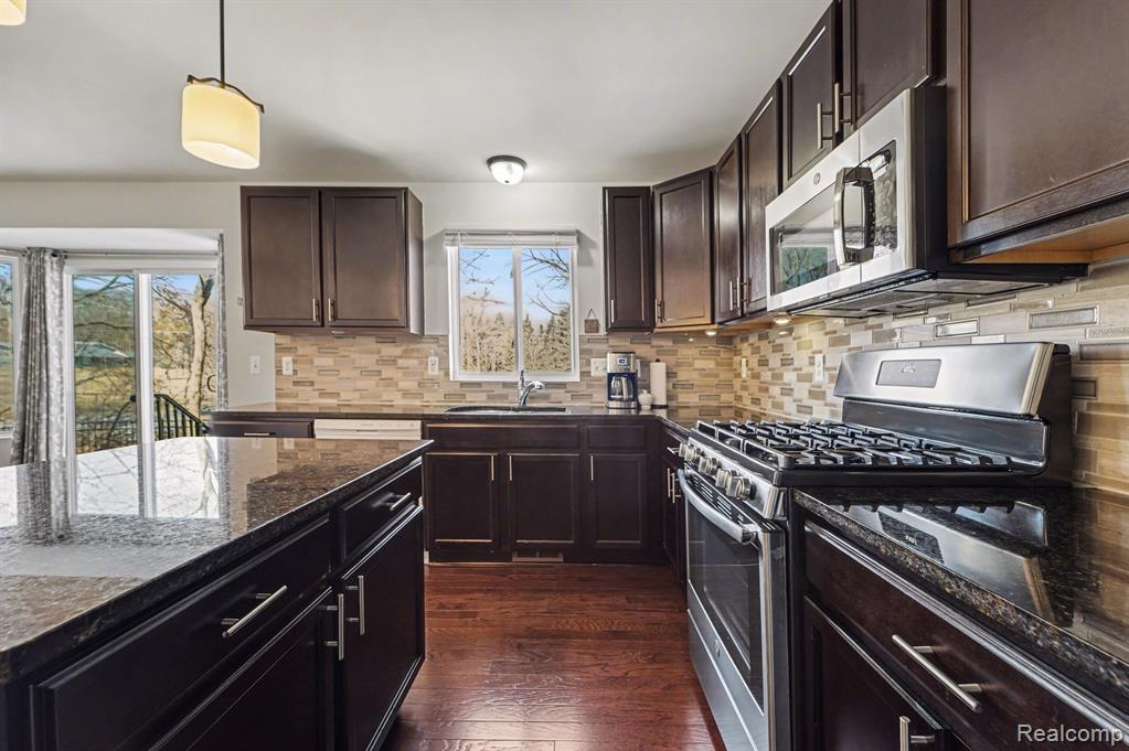 Kitchen with stainless steel appliances, dark stone countertops, dark wood-style floors, hanging light fixtures, and dark wood finish cabinets