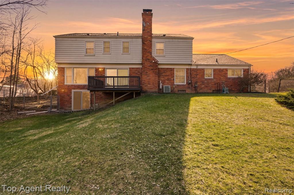 Rear view of house featuring brick siding, a deck, a lawn, and a chimney