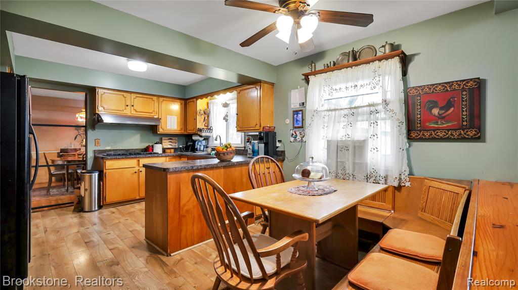 Kitchen with freestanding refrigerator, dark countertops, light wood-type flooring, ceiling fan, and wood finish cabinets