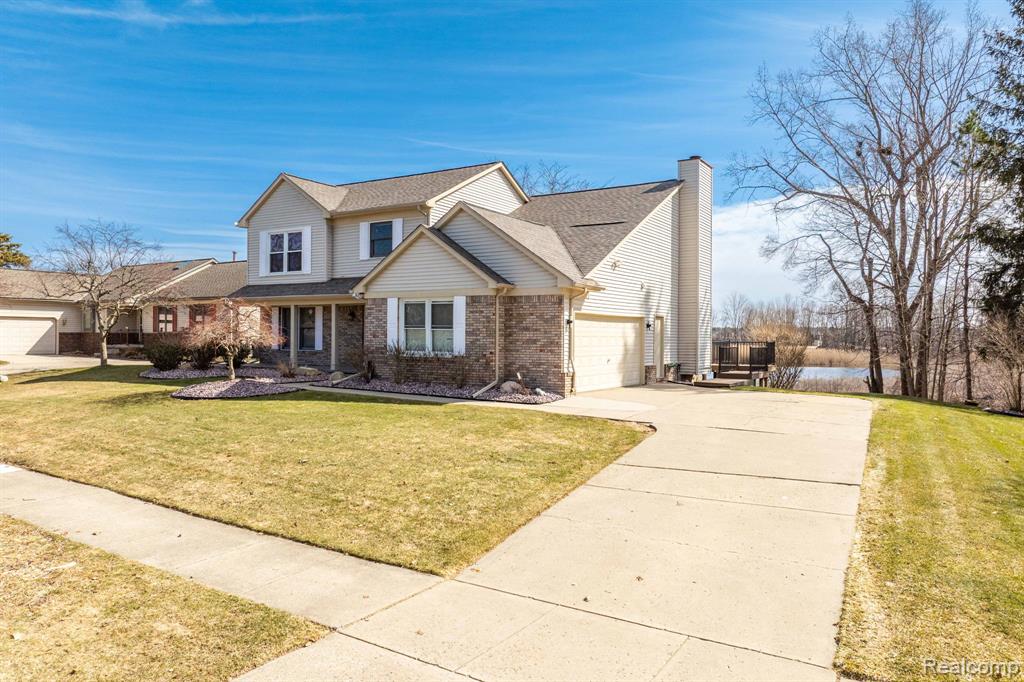 Traditional-style home with brick siding, concrete driveway, a front lawn, a chimney, and roof with shingles