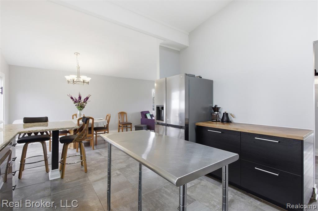 Kitchen with dark cabinets, lofted ceiling, stainless steel fridge, wood counters, and suspended lighting