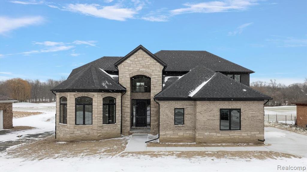French country style house featuring stone siding, roof with shingles, and brick siding