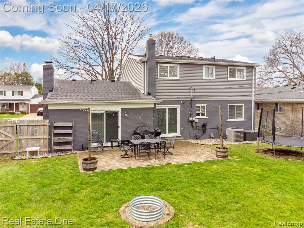 Back of house featuring a trampoline, a patio area, brick siding, a chimney, and a fenced backyard