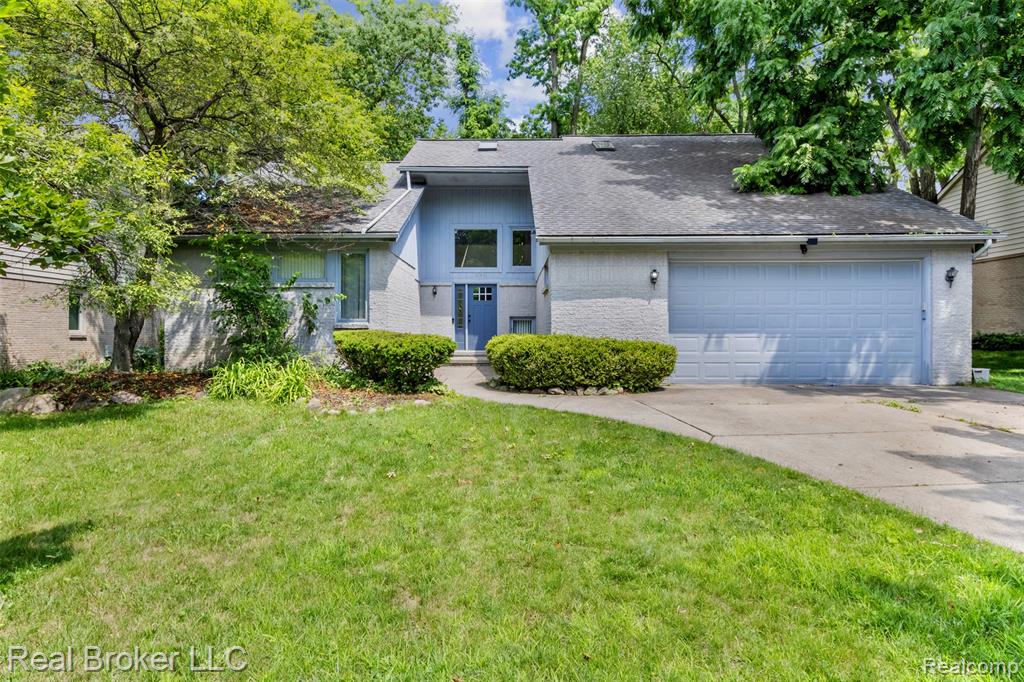 Mid-century inspired home with brick siding, a shingled roof, a front yard, a garage, and driveway