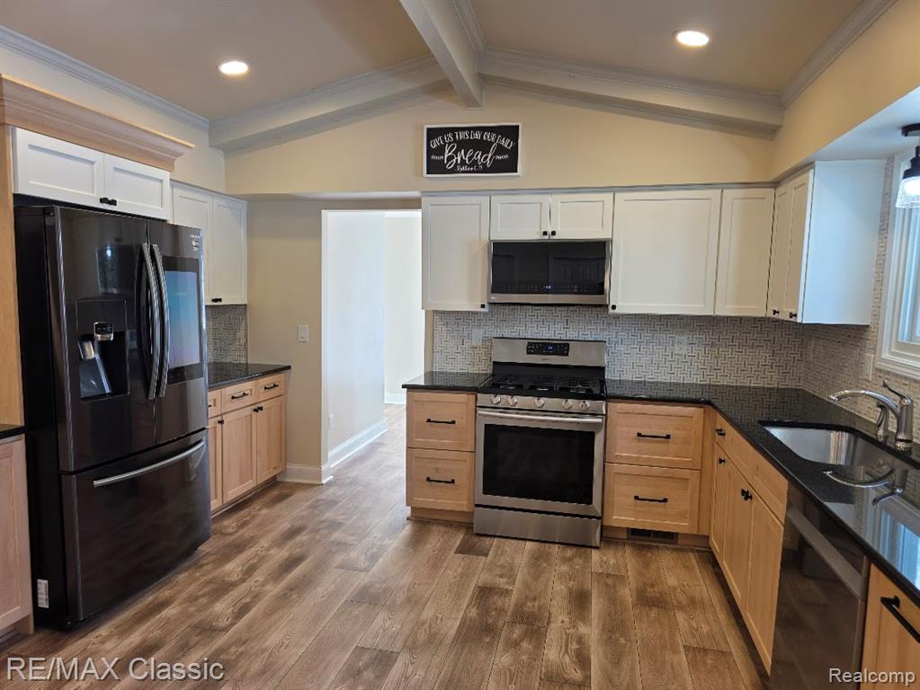 Kitchen featuring tasteful backsplash, appliances with stainless steel finishes, crown molding, dark stone countertops, and dark wood-style flooring