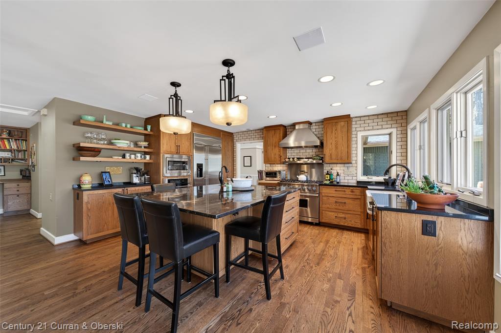 Kitchen featuring wood finish cabinetry, a breakfast bar, built in appliances, an island with sink, and backsplash
