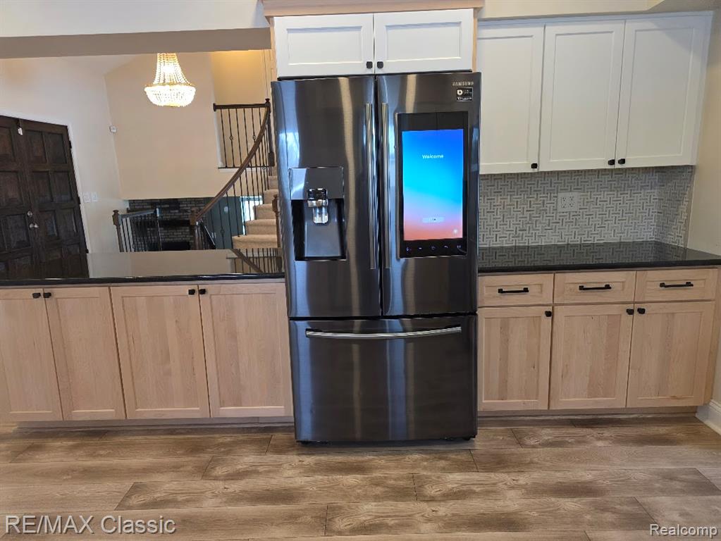 Kitchen with stainless steel fridge, decorative backsplash, light wood-type flooring, and dark stone counters