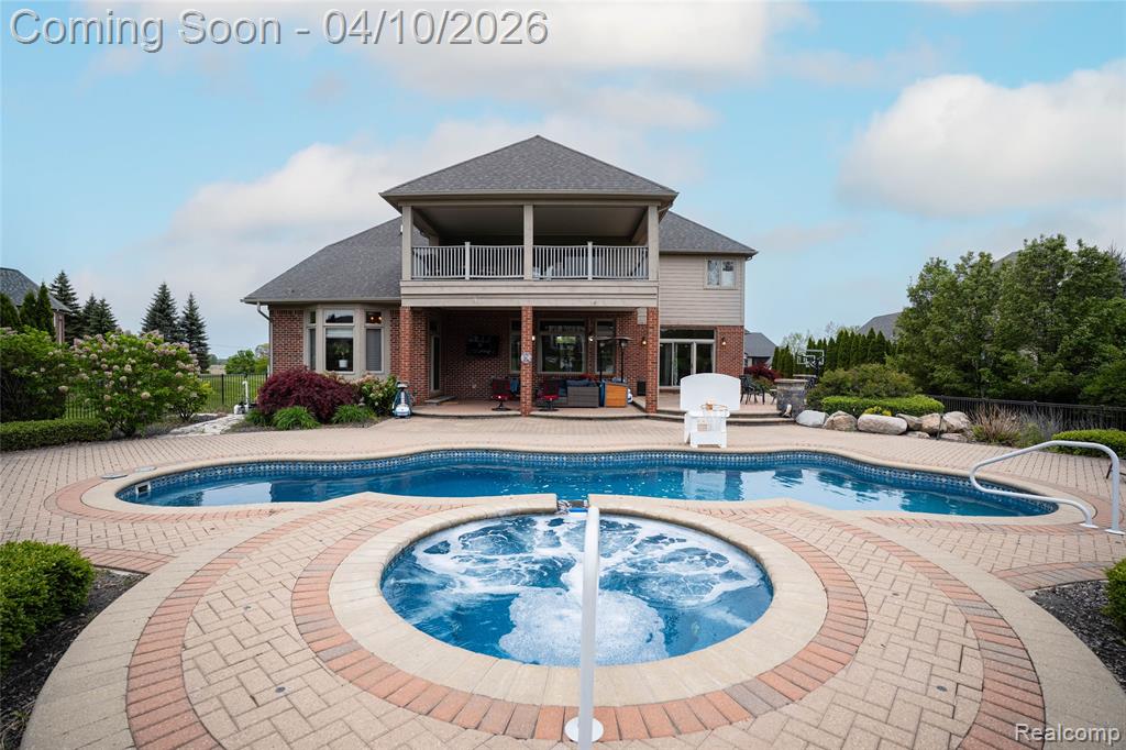 View of pool featuring an in-ground hot tub, a balcony, and patio surround