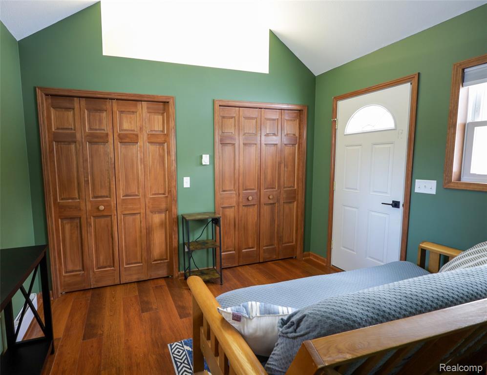Bedroom with lofted ceiling, dark wood-style floors, and multiple closets