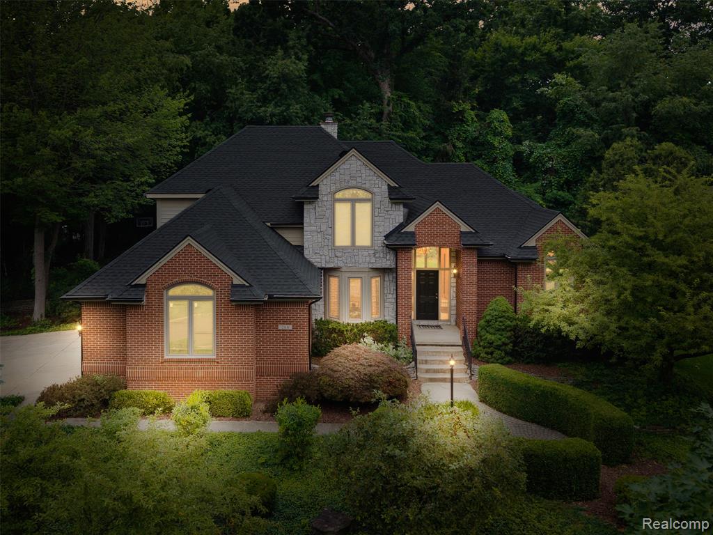 French country inspired facade with stone siding, brick siding, roof with shingles, and a forest view