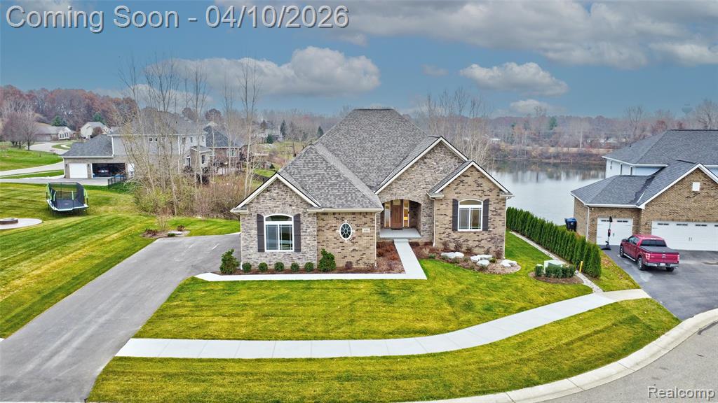 View of front of house with a front lawn, stone siding, a water view, a residential view, and driveway