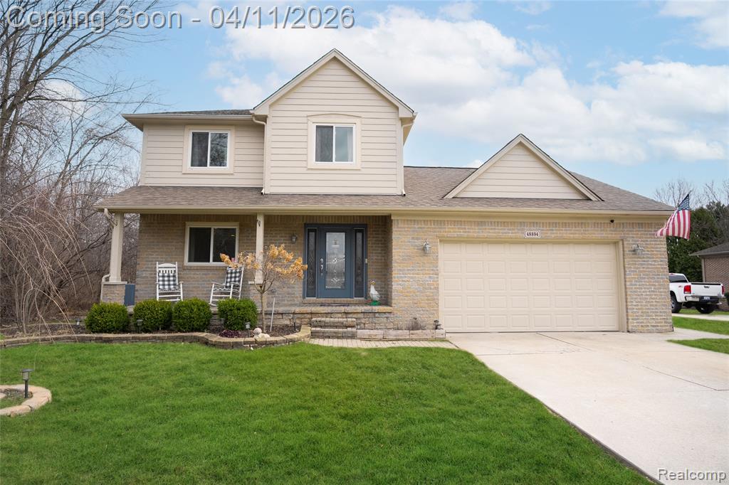 View of front of house featuring covered porch, concrete driveway, a front yard, and brick siding