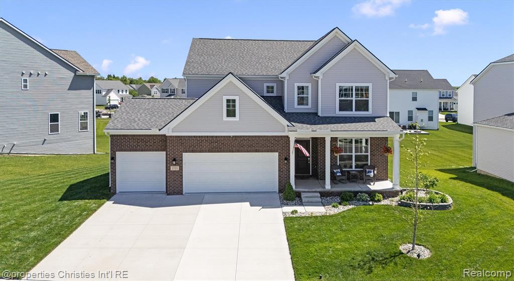 Traditional-style house with a porch, concrete driveway, a front lawn, and brick siding