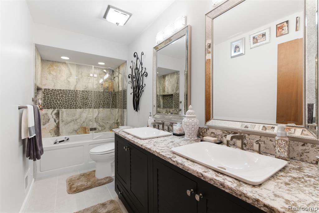 Bathroom with shower / bath combination with glass door, double vanity, and light tile patterned floors
