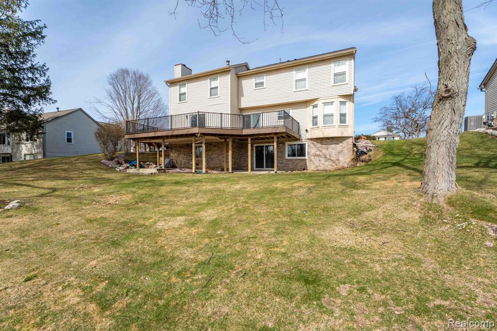 Rear view of house with a wooden deck, a chimney, a lawn, and a patio