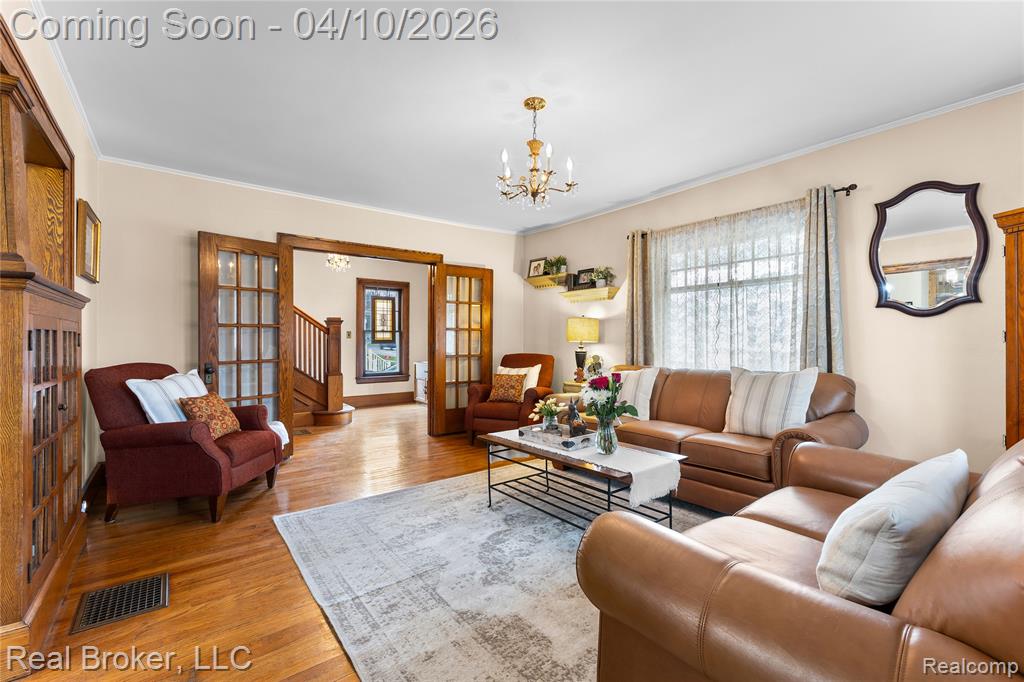 Living room featuring light wood finished floors, hanging lights, ornamental molding, and french doors