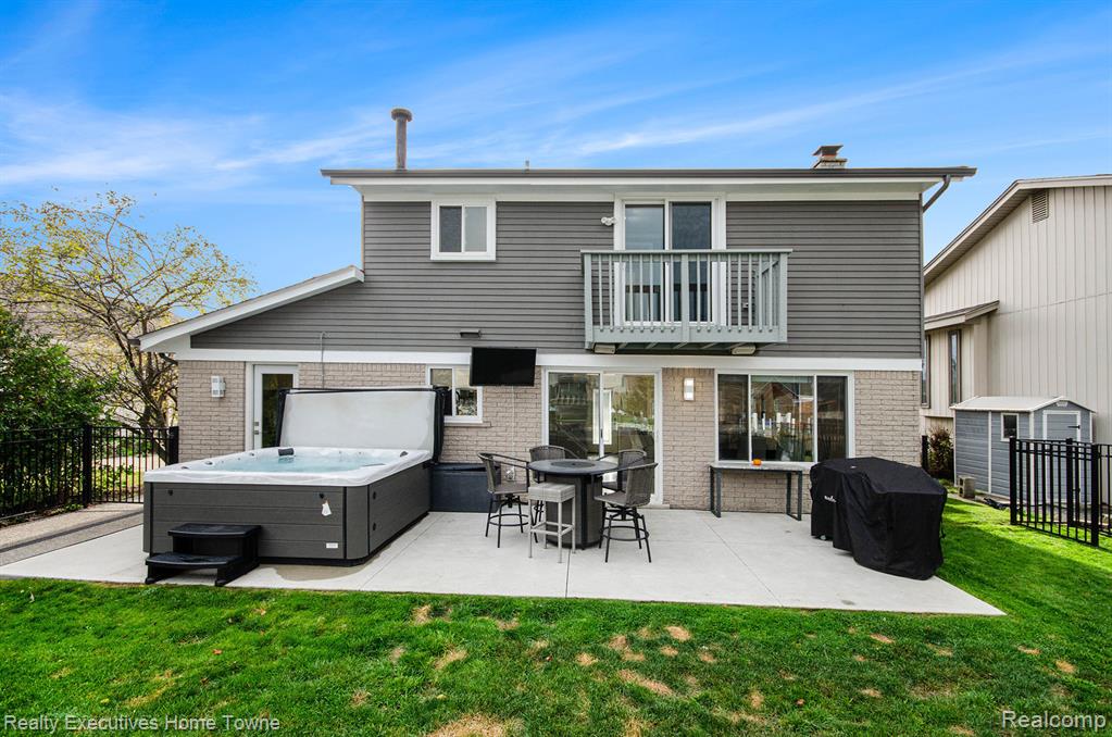 Back of house featuring brick siding, a hot tub, outdoor dining space, and a patio