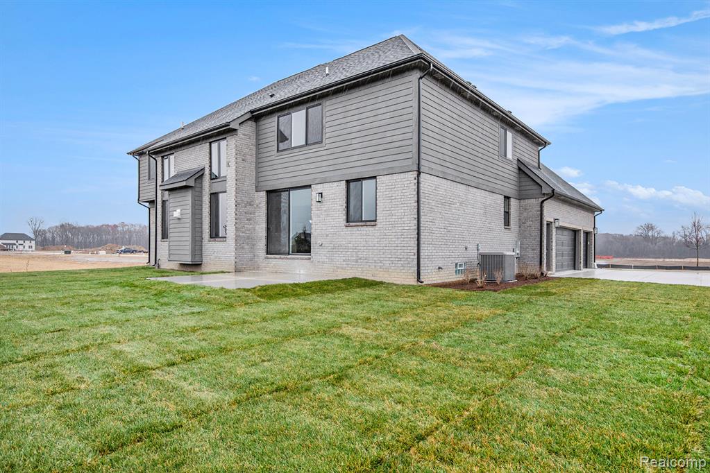 Back of house with a lawn, brick siding, driveway, and a patio
